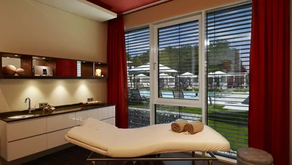 Gemütlicher Massageraum mit Fensterblick auf Außenpool und Liegestühle