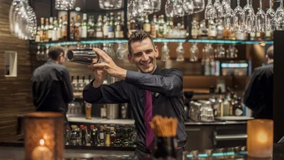 Barkeeper mixt Cocktail lächelnd hinter Bar in stilvoller Bar