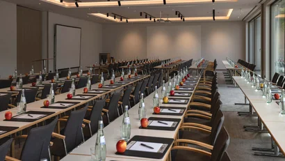 Konferenzraum mit Tischen, Stühlen, Wasserflaschen, Äpfeln und Schreibmaterial