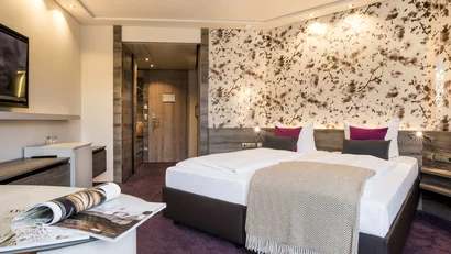 Modernes Hotelzimmer mit Doppelbett, floralem Wandmuster und offenen Zeitschriften