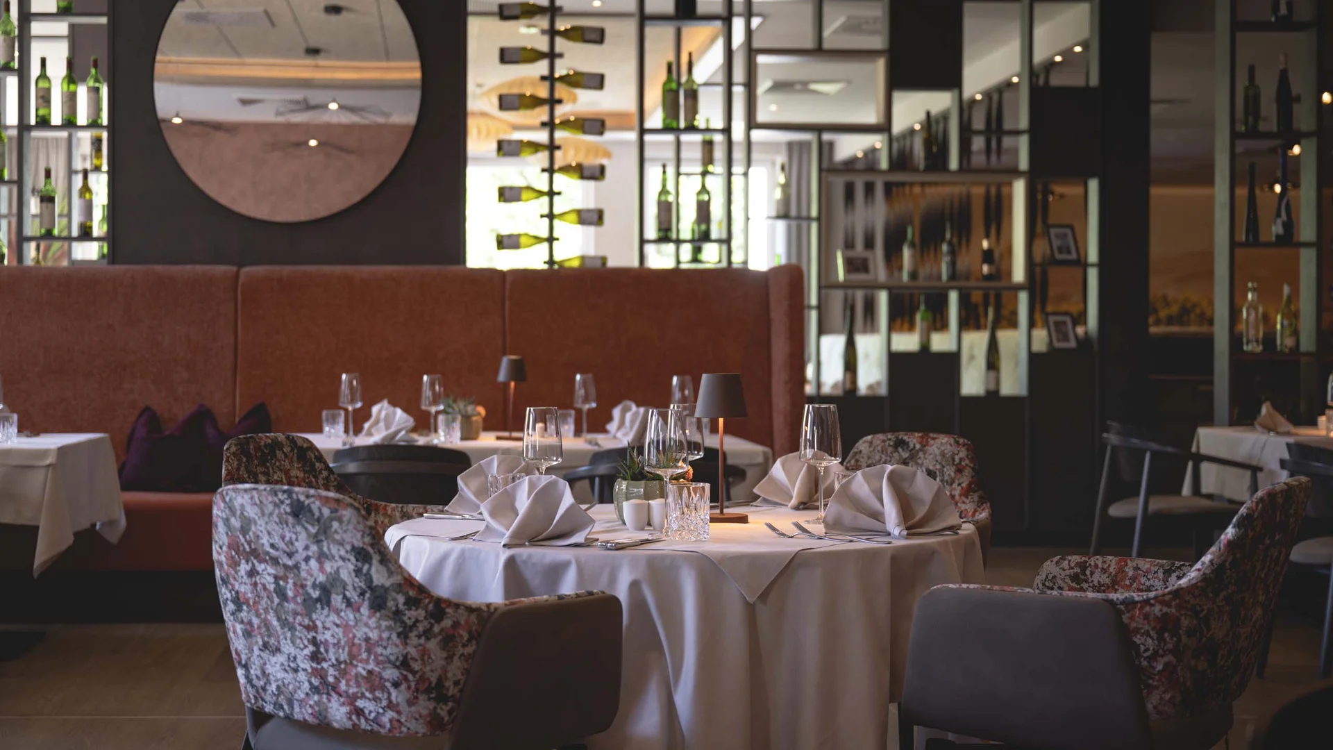 Elegantes Restaurant mit weiß gedeckten Tischen, gepolsterten Sesseln und Weinregalen