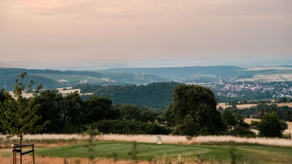Golfgrün mit Fahne vor hügeliger Landschaft und einem Dorf