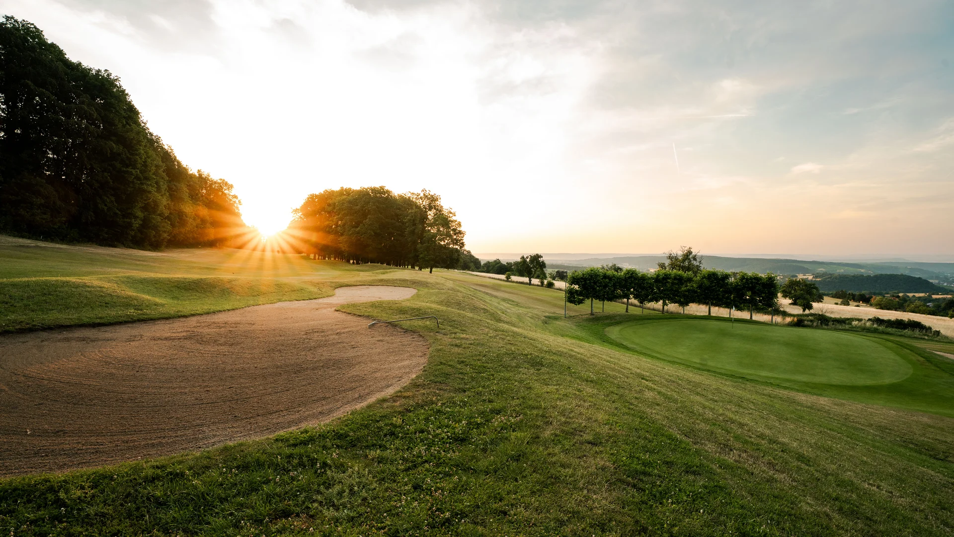 Golfplatz mit Sandbunker bei Sonnenuntergang und Blick über die Landschaft
