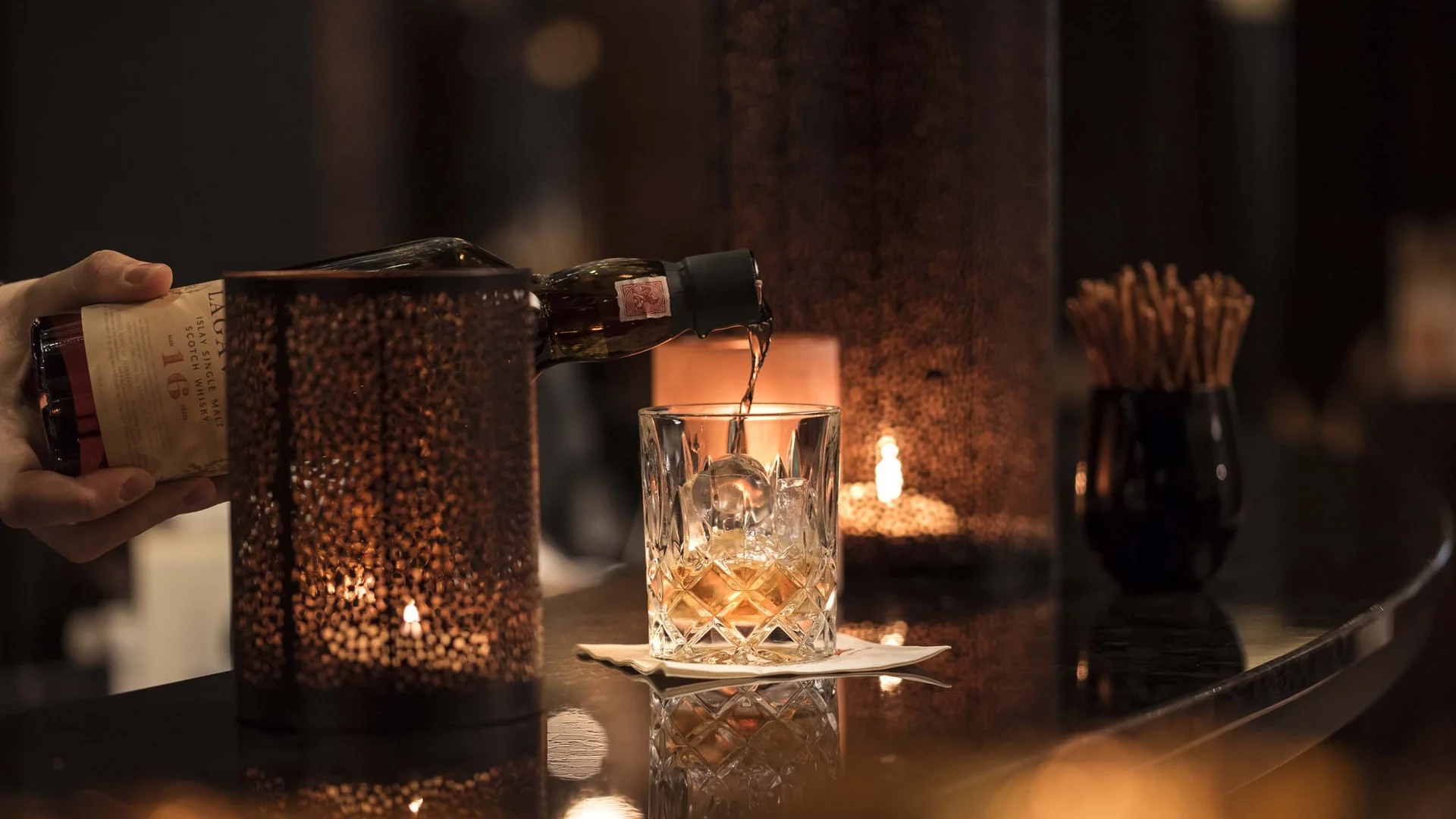 Whisky wird in ein Glas mit Eis in einer gemütlichen Bar eingeschenkt