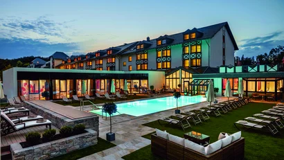 Hotel mit beleuchtetem Außenpool und Liegestühlen bei Abenddämmerung