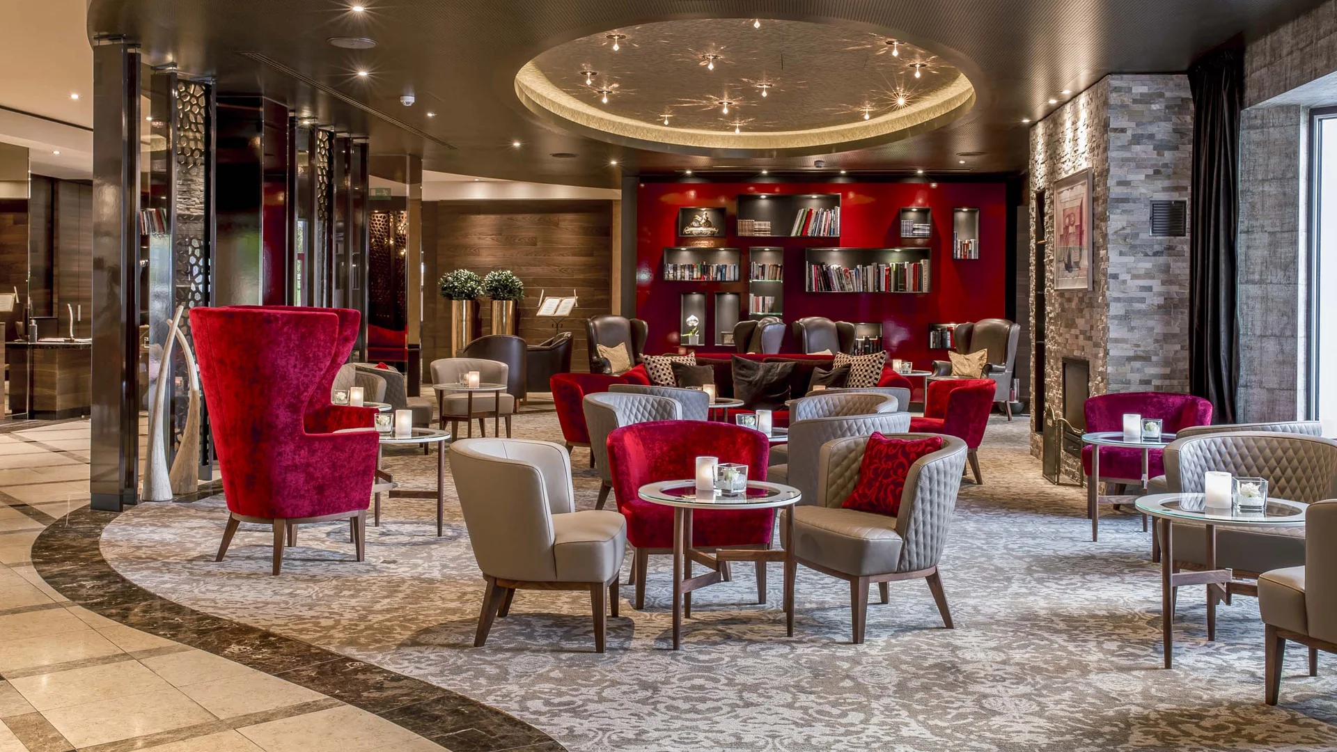 Luxuriöse Hotellounge mit roten Sesseln und Bücherregal an der Rückwand