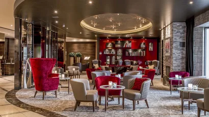 Luxuriöse Hotellounge mit roten Sesseln und Bücherregal an der Rückwand