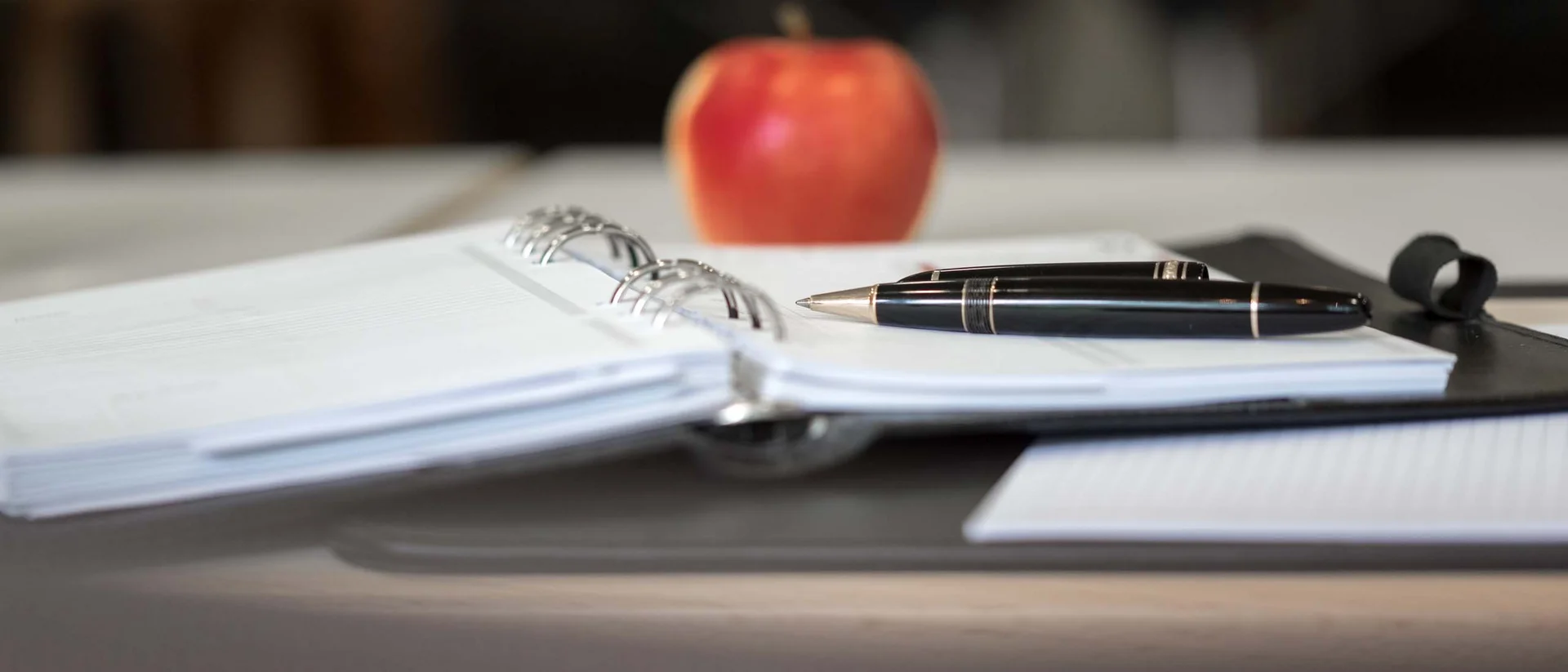 Notizbuch mit Stift und rotem Apfel auf einem Tisch