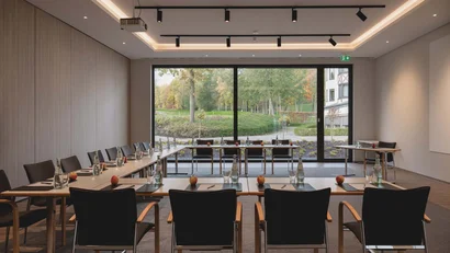 Moderner Konferenzraum mit Stühlen, Tischen, Bottles und Fensterblick auf Grünfläche