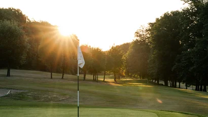 Golfplatz mit Fahne bei Sonnenaufgang und bewaldeter Umgebung