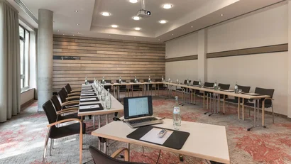 Konferenzraum mit U-förmigem Tisch, Stühlen, Laptop und Wasserflaschen