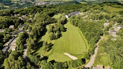 Luftaufnahme eines Golfplatzes umgeben von Wald und Wohnhäusern