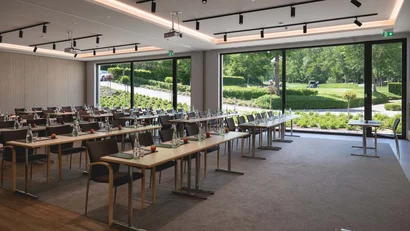 Konferenzraum mit Tischen, Stühlen und großen Fenstern mit Blick ins Grüne