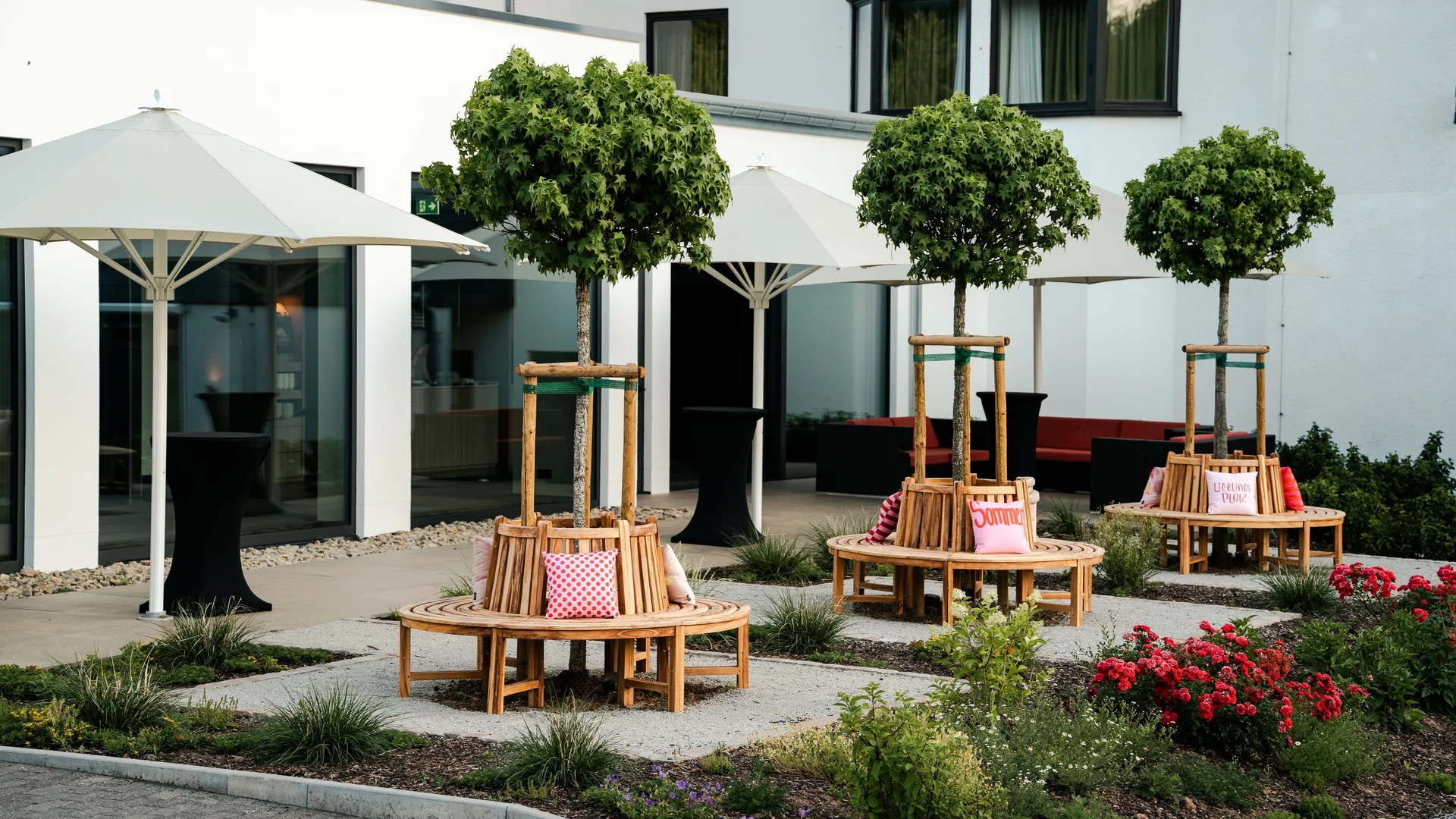 Hotelhof mit Sonnenschirmen, Sitzbänken, kugelförmigen Bäumen und Blumenbeeten