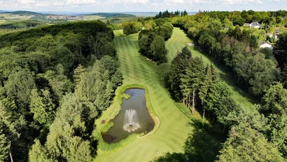 Luftaufnahme eines Golfplatzes mit Teich und Springbrunnen umgeben von Bäumen