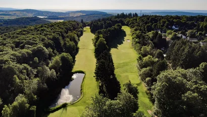 Luftaufnahme eines Golfplatzes mit Wasserhindernis und umliegendem Wald