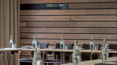 Tagungsraum mit Tischen, Stühlen und Wasserflaschen vor Holzwand