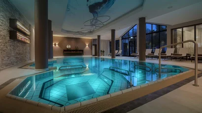 Innenpool mit türkisfarbenem Wasser, Liegestühlen und Kamin