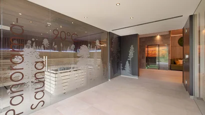 Heller Spa-Eingang mit Glaswand, Waldmotiven und Blick auf einen gemütlichen Sitzbereich