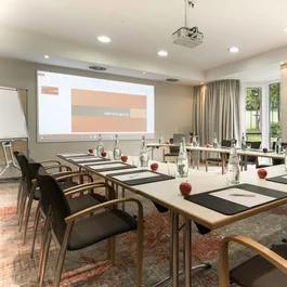 Konferenzraum mit U-förmigen Tischen, Stühlen, Wasserflaschen und roten Äpfeln