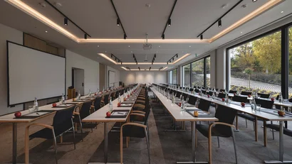 Moderner, heller Konferenzraum mit langen Tischen, Stühlen und Fenstern