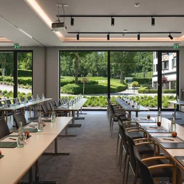 Konferenzraum mit Tischen, Stühlen und Blick auf grüne Außenanlage