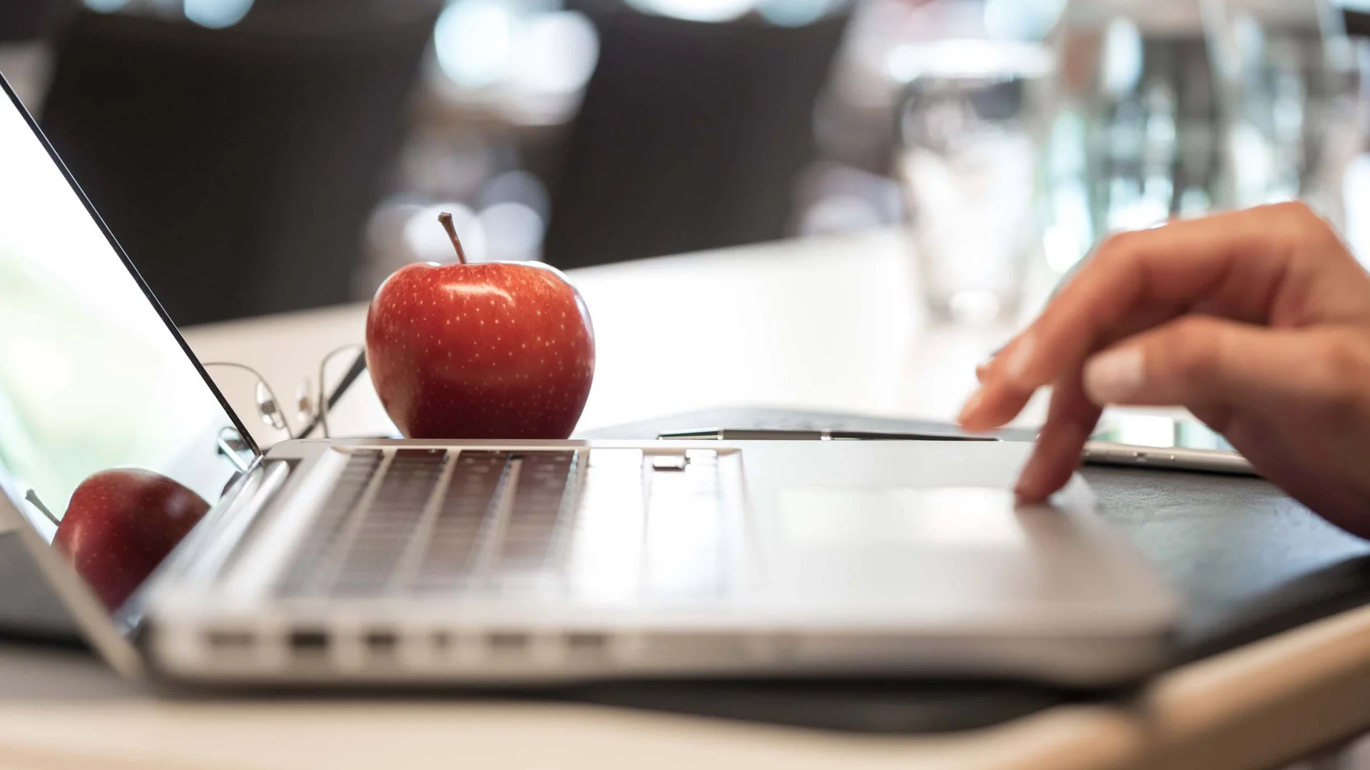 Roter Apfel auf Laptop mit Hand auf Touchpad in Büro