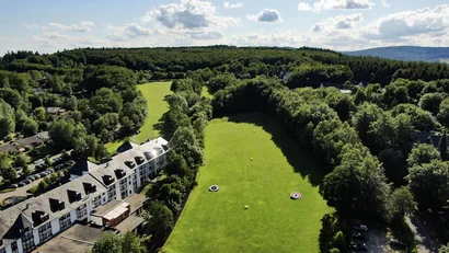 Luftaufnahme eines grünen Golfplatzes neben einem großen Hotelgebäude und Wald