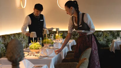 Zwei Kellner richten im Restaurant Tische mit weißen Tüchern und Blumen ein