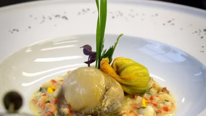 Fein angerichtetes Gericht mit Muschel und essbarem Blütenblatt auf Gemüsesauce