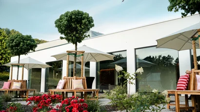 Moderner weißer Bau mit Sitzbänken, Sonnenschirmen und blühendem Garten