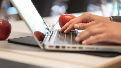 Hände tippen auf Laptop-Tastatur mit Äpfeln im Hintergrund