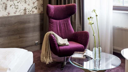 Lila Sessel mit beige Decke neben Glas-Tisch mit Blumen und Magazin im Zimmer