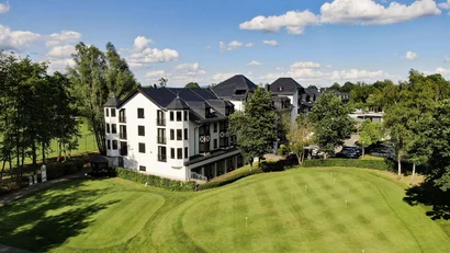 Hotel neben Golfübungsplatz mit mehreren Fahnen bei sonnigem Wetter