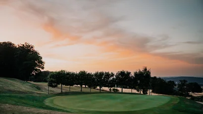 Golfgrün mit Bäumen und orangefarbenem Abendhimmel